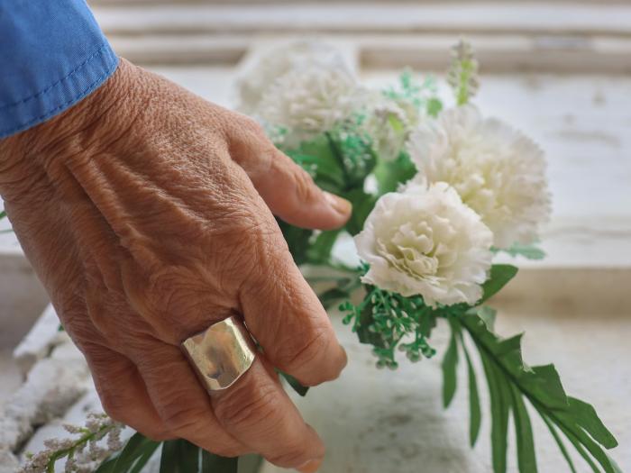 Gammal människars hand som lägger ner vita blommor på en kista.